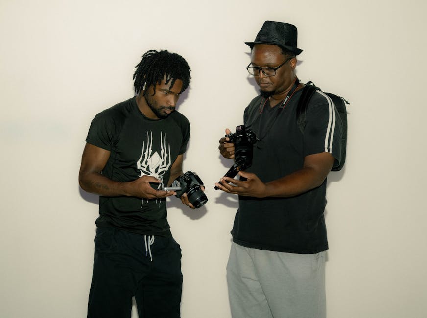 Two photographers indoors discussing and examining cameras passionately, fostering collaboration and learning.